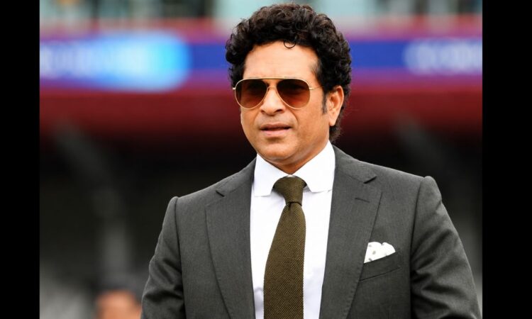 Sachin Tendulkar in a formal black suit and sunglasses at a cricket stadium during a public appearance.